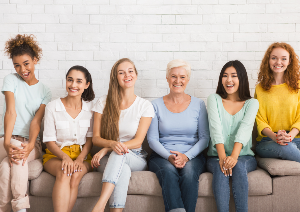 Women of different ages, unique skin tones and clothes sit on a lounge together